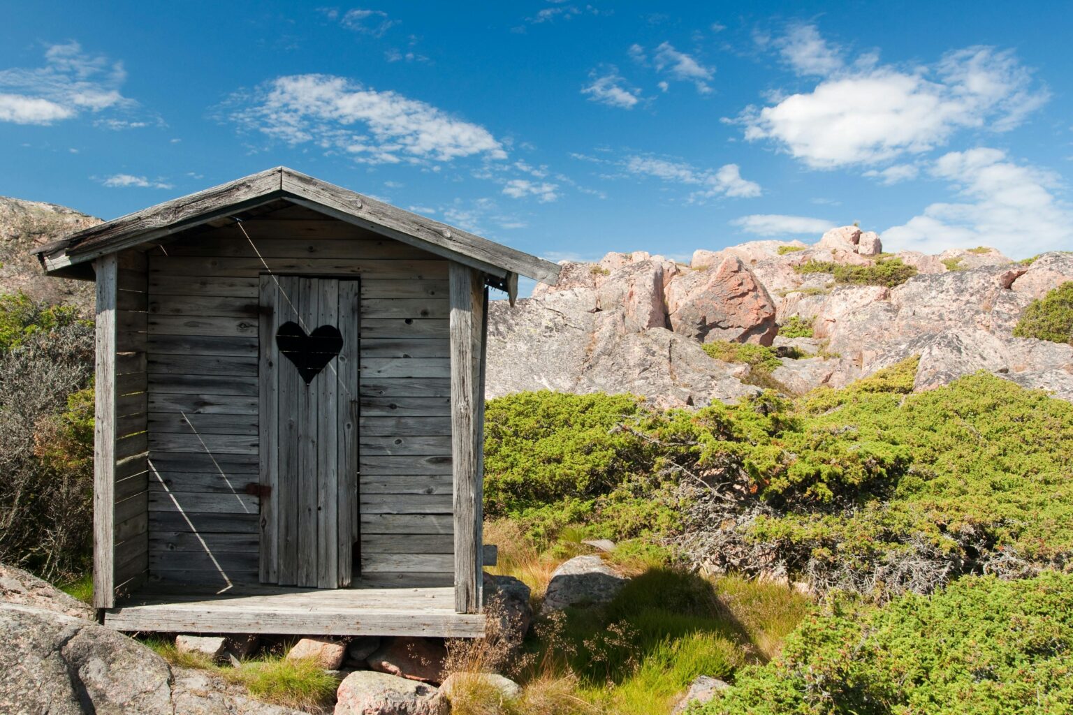 Charming rustic wooden cabin with heart-shaped door in rocky countryside.
